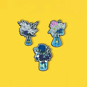 Detailed view of three enamel flower pins in chemical flasks on a yellow background