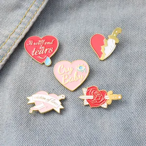 Detail of five enamel pins with heart and letter designs on blue denim fabric