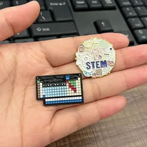 Detalle de pines de esmalte de Women in STEM y Tabla Periódica sostenidos en la mano