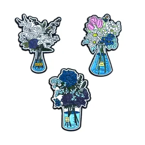 Detailed macro view of three artistic floral enamel pins in blue laboratory glassware