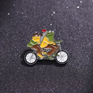 Détail d'une broche en émail représentant des grenouilles en tandem avec un cœur rouge