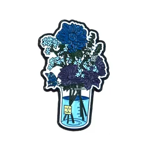 Detail of an enamel pin featuring colorful flowers inside a chemical beaker with yellow label