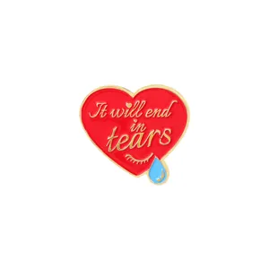 Close-up of heart enamel pin with gold lettering It will end in tears and blue teardrop