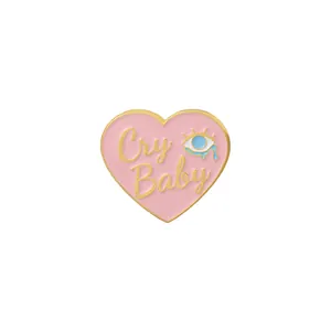 Detail of pink heart enamel brooch featuring gold Cry Baby text and a blue teardrop eye