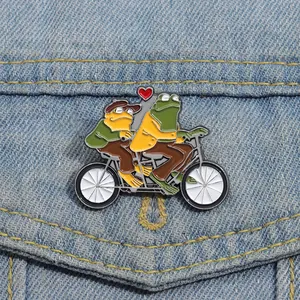 Détail du pin's Frog and Toad sur denim, roulant sur un tandem avec un motif de cœur