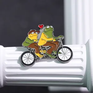 Détail du pin's émaillé grenouille et crapaud à vélo sur un présentoir colonne blanc