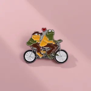 Détail du pin's émaillé montrant deux grenouilles sur un tandem avec un cœur décor