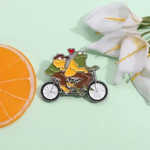 Détail de deux grenouilles en émail sur un tandem, posées sur un fond vert pastel