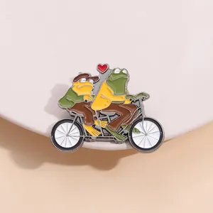 Détail de l'épinglette en émail représentant un crapaud et une grenouille à tandem
