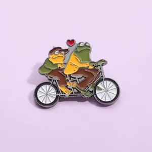 Détail d'un pin's émaillé montrant deux grenouilles sur un tandem avec un petit cœur