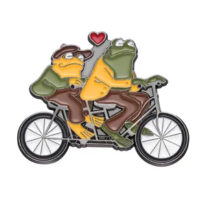 Broche en émail représentant deux grenouilles sur un tandem avec un décor de cœur rouge