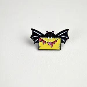 Cartoon bat enamel pin holding yellow envelope with pink heart and red blood droplets