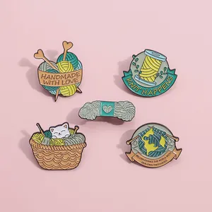 Gros plan de broches en émail avec chats et pelotes de laine sur fond rose tendre