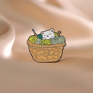 Détail d'une épingle en émail avec un chat dans un panier de laine sur de la soie