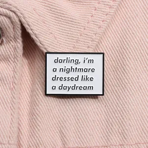 Close-up of a rectangular enamel letter badge pinned on pink denim jacket fabric