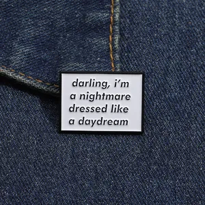 Close-up of rectangular enamel brooch with quote pinned on blue denim fabric texture