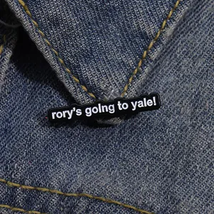 Detailopname van een zwarte emaille speld met tekst Rory's Going to Yale op denim