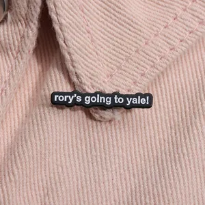 Zwarte emaille pin met rory's going to yale tekst op een roze spijkerjasje kraag