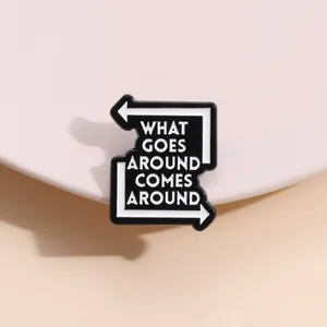 Detailed close-up of enamel brooch with What Goes Around Comes Around text in black and white