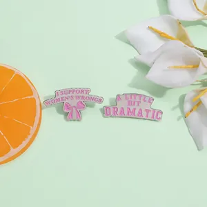 Détail de pin's en émail rose avec slogans féminins et nœud sur fond vert clair rafraîchissant