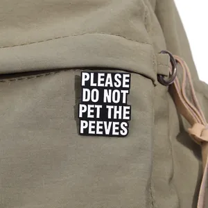 Detail view of the black enamel pin featuring funny text on a green canvas background