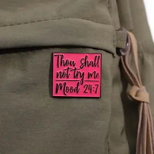 Pink enamel brooch with 24/7 mood text pinned on a green canvas backpack accessory