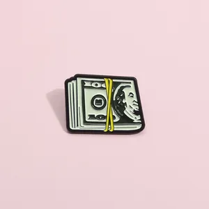 Gros plan détaillé d'un pin's émaillé en forme de liasse de 100 dollars avec ruban jaune