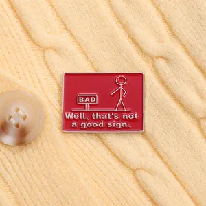 Close-up of a red enamel stickman pin with humorous text on yellow knit fabric