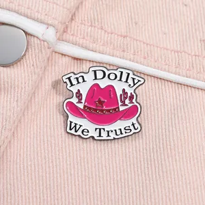 Detail of pink cowboy hat enamel pin with In Dolly We Trust text on denim fabric