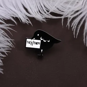 Close-up of black bird enamel pin with They/Them pronouns on dark background