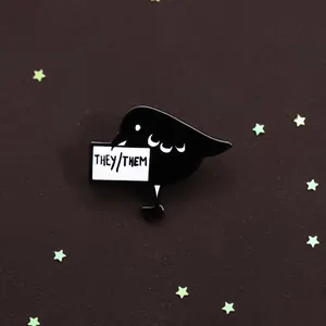 Macro view of black bird enamel pin with They/Them pronouns sign on dark textured surface