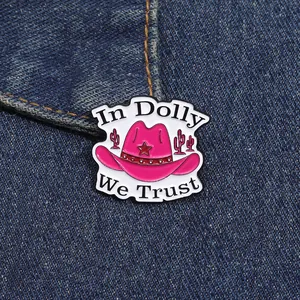 Detail of pink cowboy hat enamel pin with In Dolly We Trust text on denim fabric