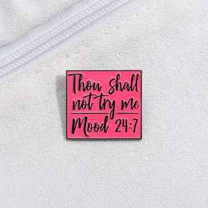 Detail of square pink enamel pin with 'Thou shall not try me' text on white canvas