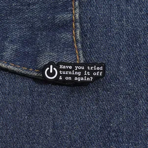 Détail d'un pin's émaillé noir avec citation geek sur le rebord d'une poche en jean