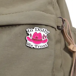 Detail of pink enamel cowboy hat brooch pinned on a khaki canvas bag with logo In Dolly We Trust