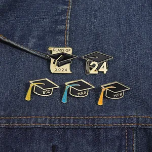Detailed view of five 2024 graduation enamel pins with bachelor caps on denim fabric