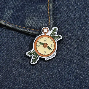 Close-up of enamel compass brooch with floral design and Jeremiah 29:11 on denim fabric