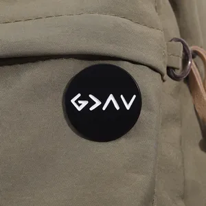 Close-up of black enamel pin with white symbols on olive green canvas bag pocket