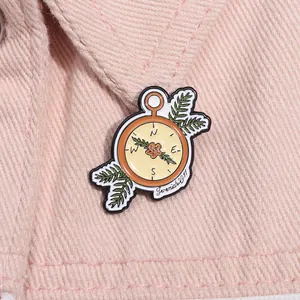 Macro detail of enamel compass brooch with Jeremiah 29:11 text on pink denim fabric