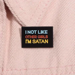 Close-up of rectangular black enamel pin with I'M SATAN text on pink denim fabric