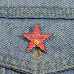 Detail of red glitter star enamel pin with Jesus Christ text on denim fabric