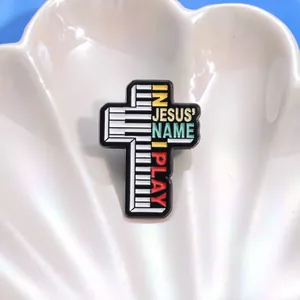 Détail du pin's émaillé en forme de croix avec touches de piano et texte sacré