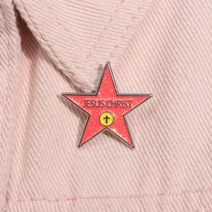 Detail of red glitter pentagram brooch with Jesus Christ text on pink denim fabric