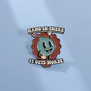 Macro detail of enamel pin showing a cartoon bomb character with humorous phrases