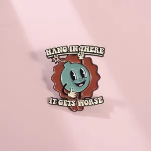 Detail of cartoon bomb enamel pin with Hang In There text and vintage metal texture