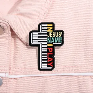 Détail de la broche croix en émail avec touches de piano et texte In Jesus Name I Play