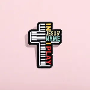 Détail du pin's émaillé en forme de croix avec touches de piano et texte religieux