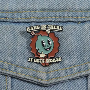 Macro shot of an enamel metal pin with Hang In There text on a blue denim jacket texture