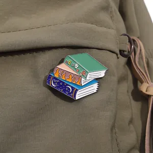Macro shot of three stacked fantasy book enamel pins on an olive green canvas bag