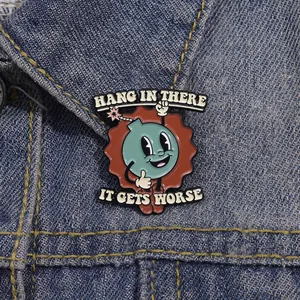 Detail of cartoon bomb enamel pin with 'Hang in there' text on a blue denim jacket collar